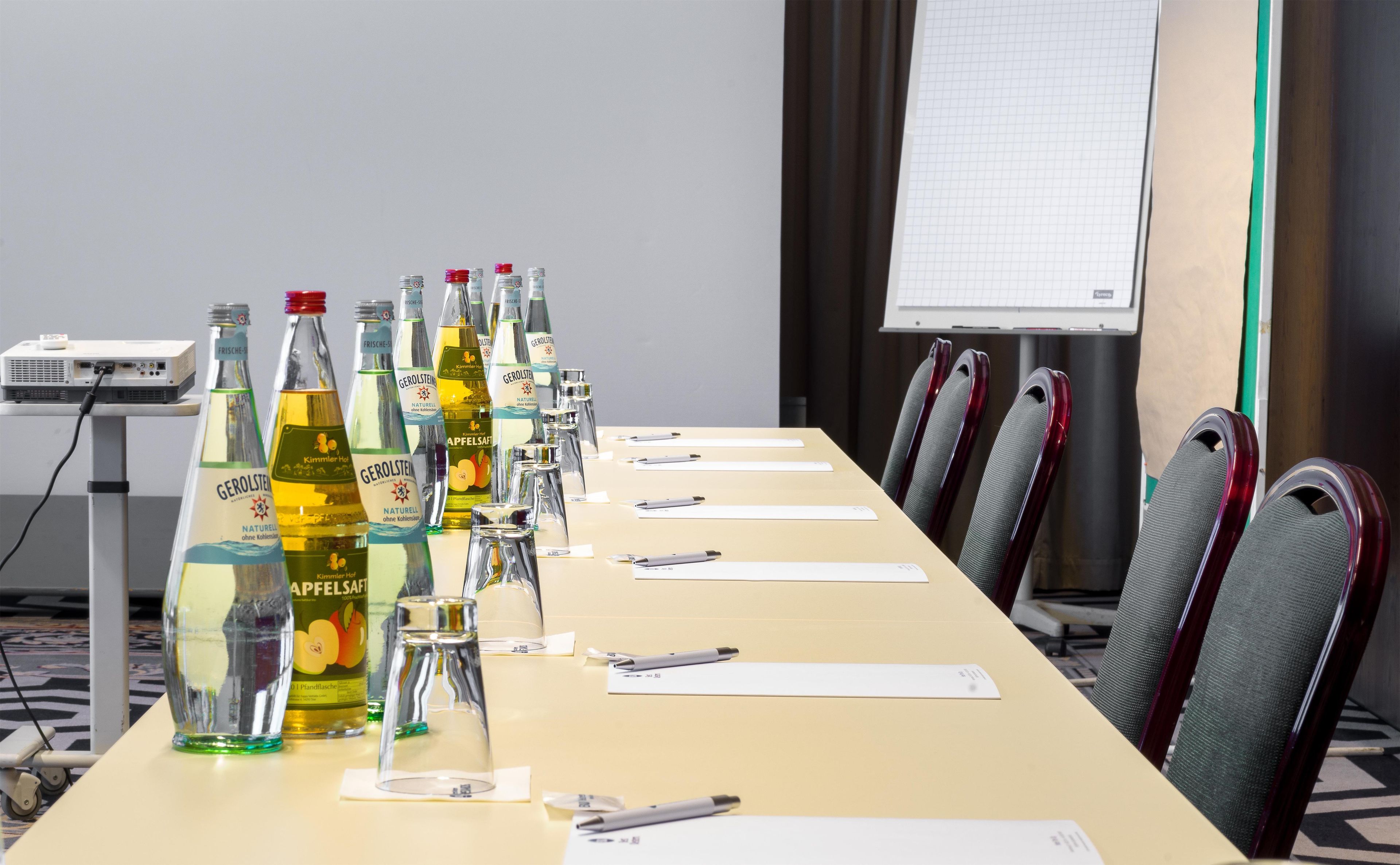 Un salón de conferencias con una mesa larga, varias botellas de cerveza Gerolsteiner, vasos, bolígrafos y tarjetas de identificación.