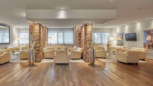 A spacious room with a modern design, featuring a central seating area with multiple sofas and a large screen on the wall.