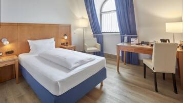A hotel room with a bed, bedside tables, a desk, a chair, and a window with curtains.