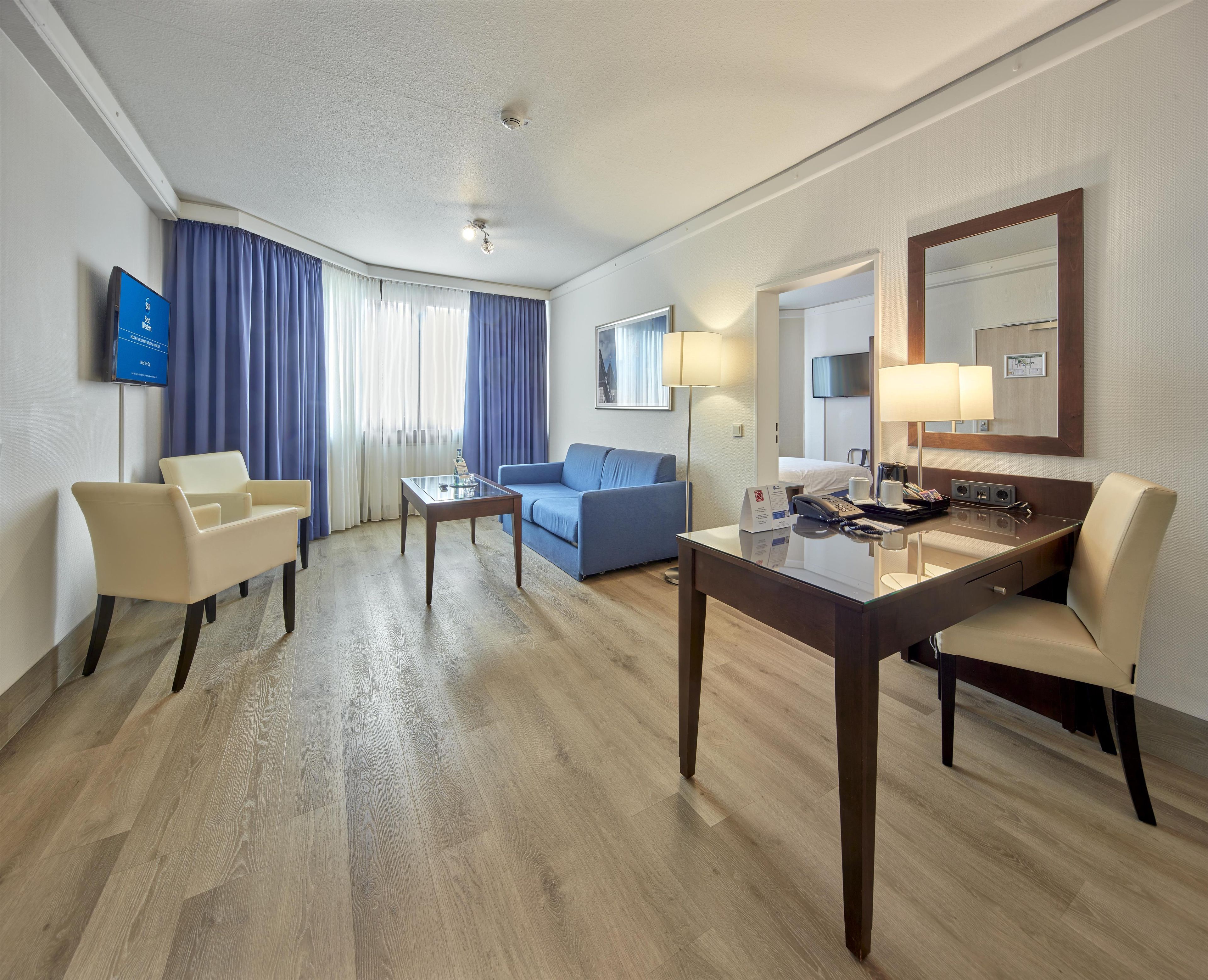 Habitació d'hotel amb televisió de pantalla plana, un sofà, escriptori amb telèfon i un mirall.