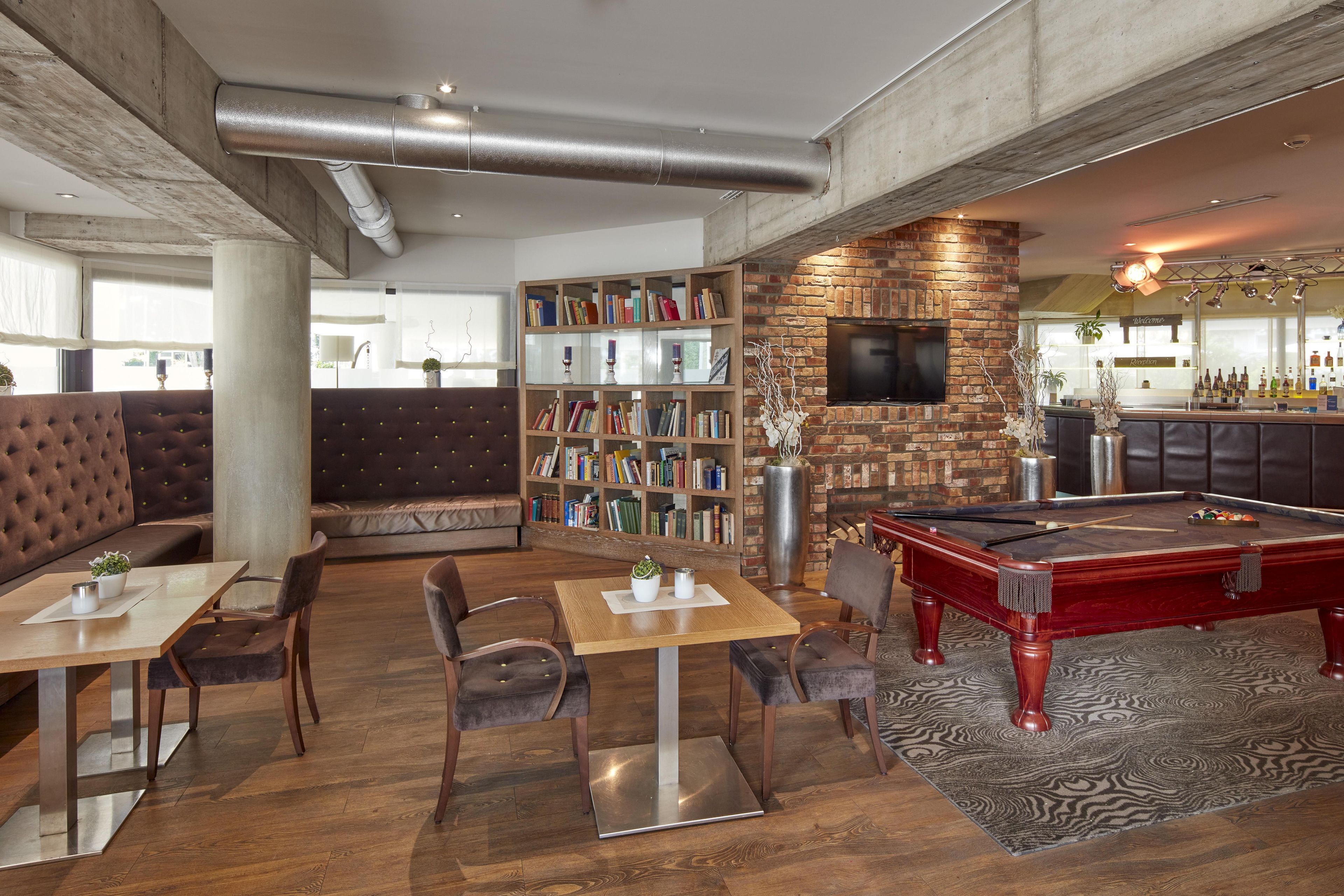 A lounge area with a pool table, seating, and a bookshelf.