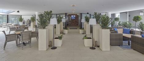 A hotel lobby with a central seating area, potted plants, and a reception desk.