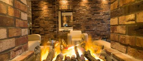 A fireplace with logs, a sofa, and a brick wall.