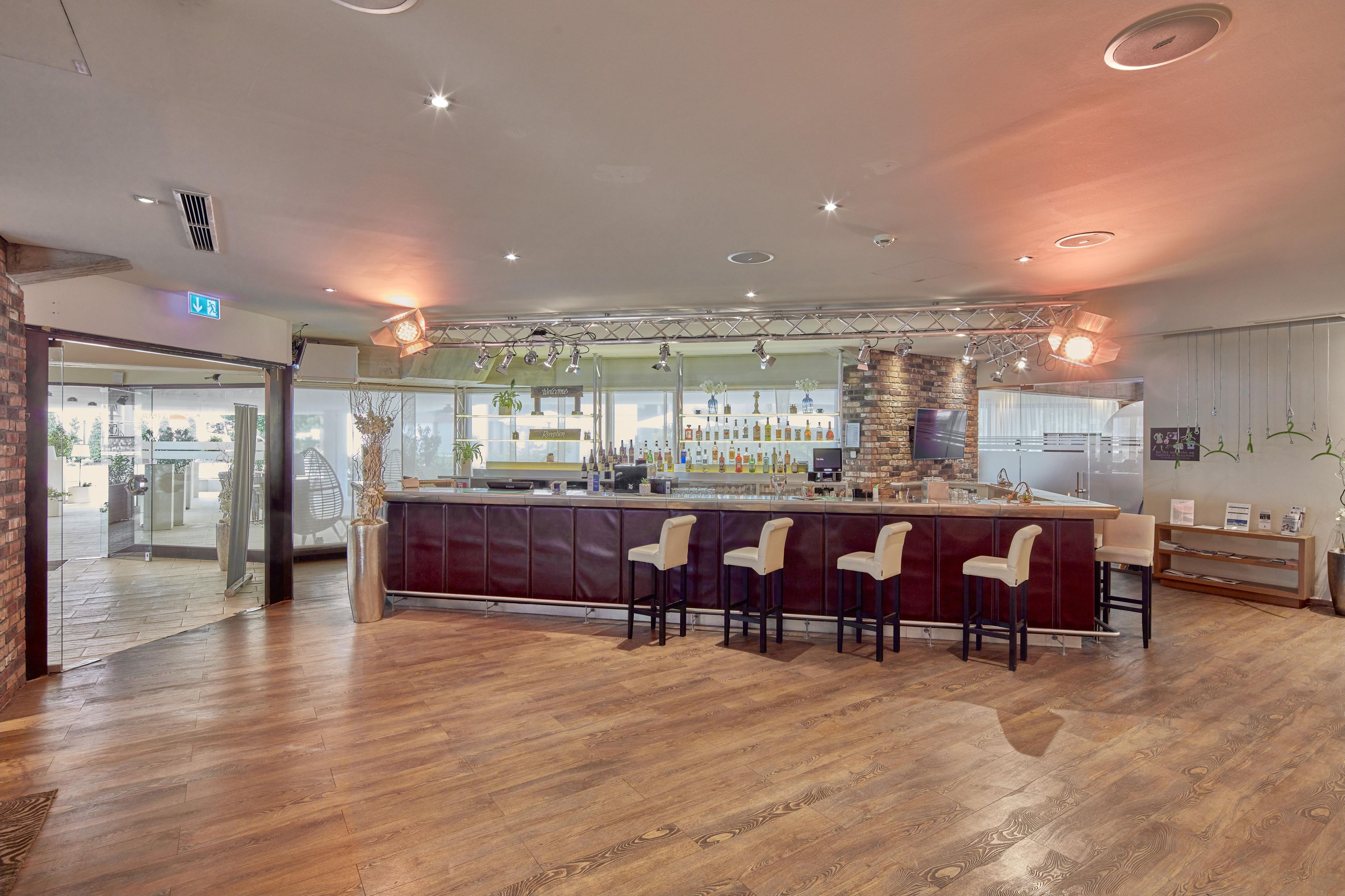 A bar area with wooden flooring, a reception desk, and bar stools.