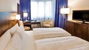 Une chambre d’hôtel avec un grand lit, un bureau avec une chaise, une télévision et un minibar.