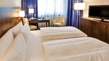 A hotel room with a large bed, a desk with a chair, a television, and a minibar.