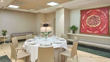 A conference room with a round table set for a meeting, a large red painting on the wall, and a potted plant on a shelf.