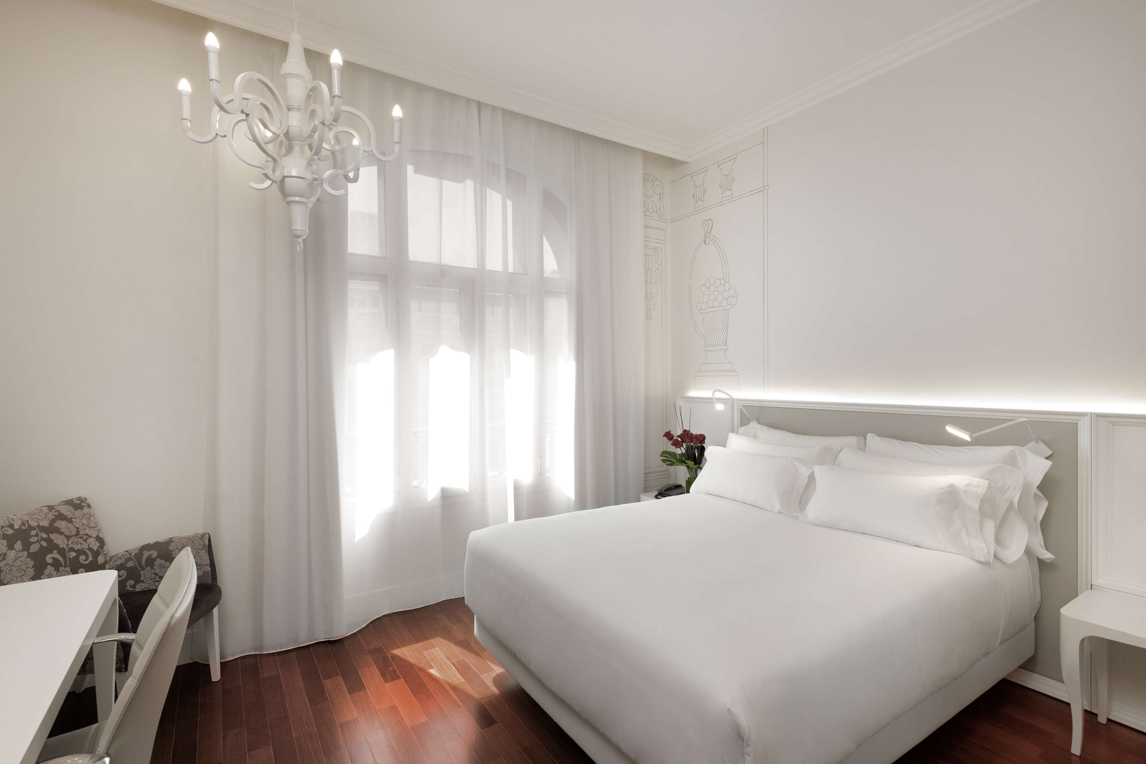 A bedroom with a large bed, a bedside table, a desk, and a chandelier.