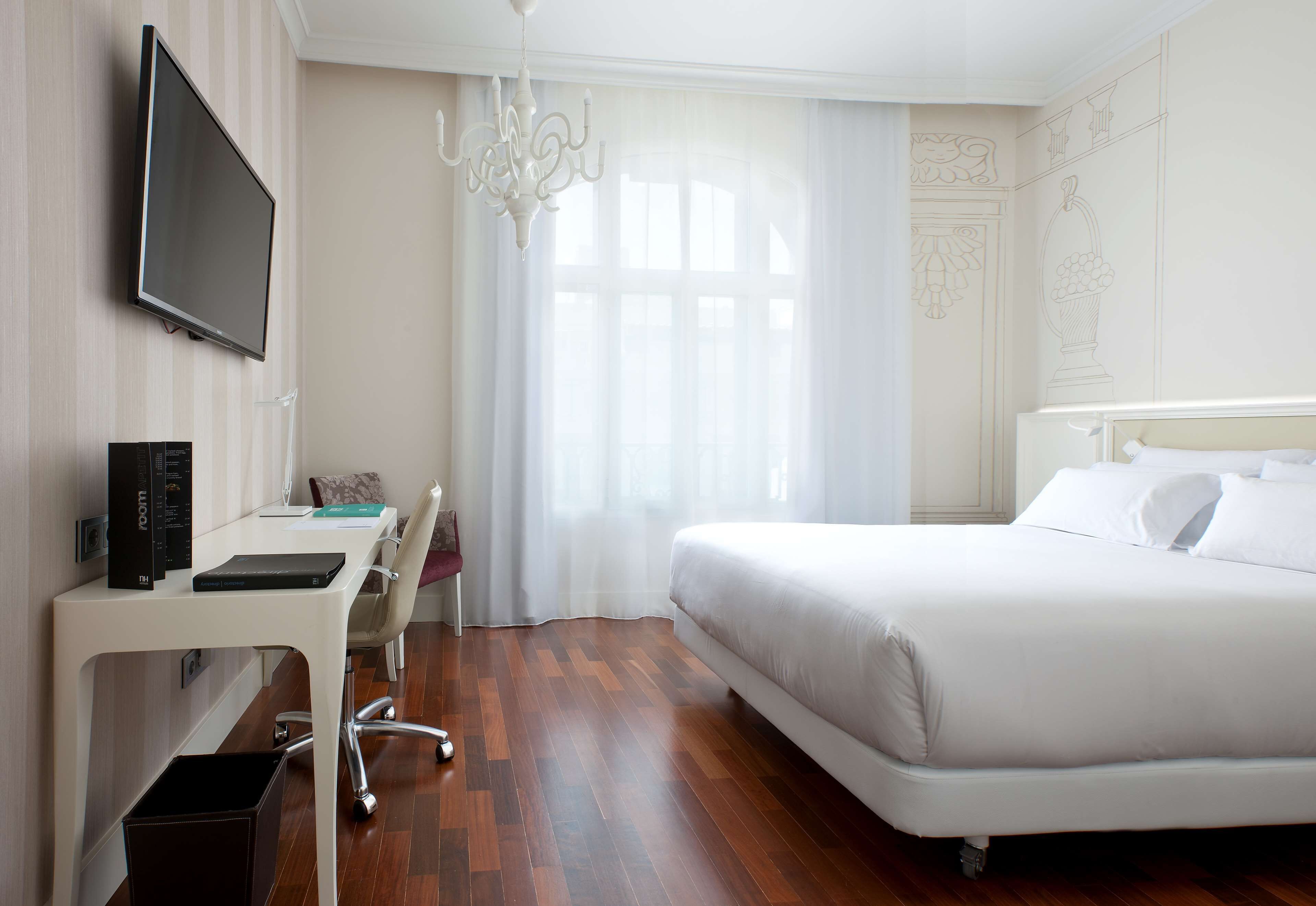 Habitació d'hotel amb un llit, un escriptori amb un ordinador, un televisor i un penjador de cristall.