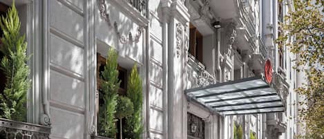 A grand building with classical architecture, featuring ornate columns, balconies, and a prominent entrance with a glass canopy.