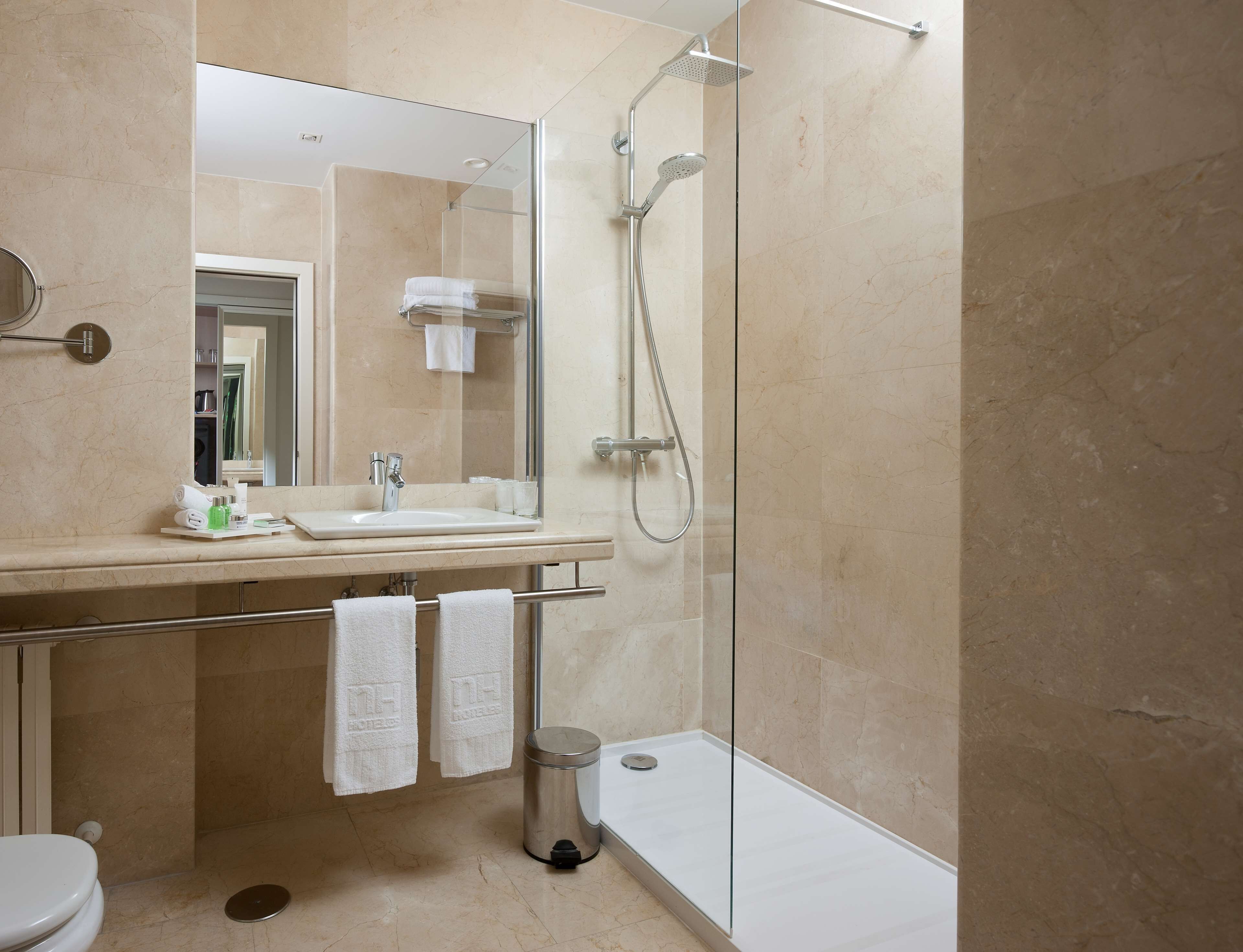 Bany modern amb dutxa envidriada, un lavabo amb mirall i dues tovalloles penjades d'una barra.