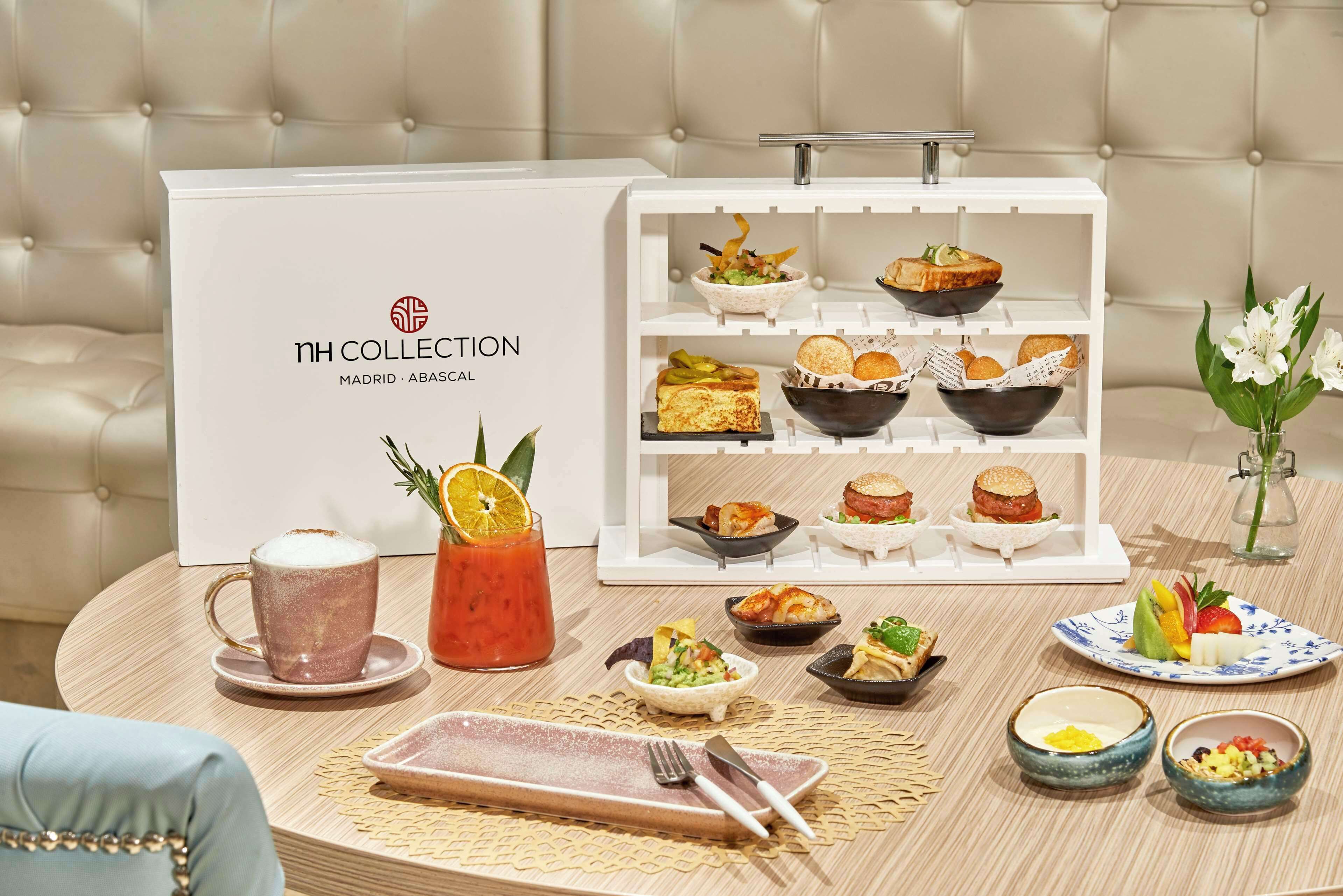 Una mesa blanca con alimentos varios y una caja blanca con la etiqueta 'nh COLLECTION MADRID - ABASCAL'.
