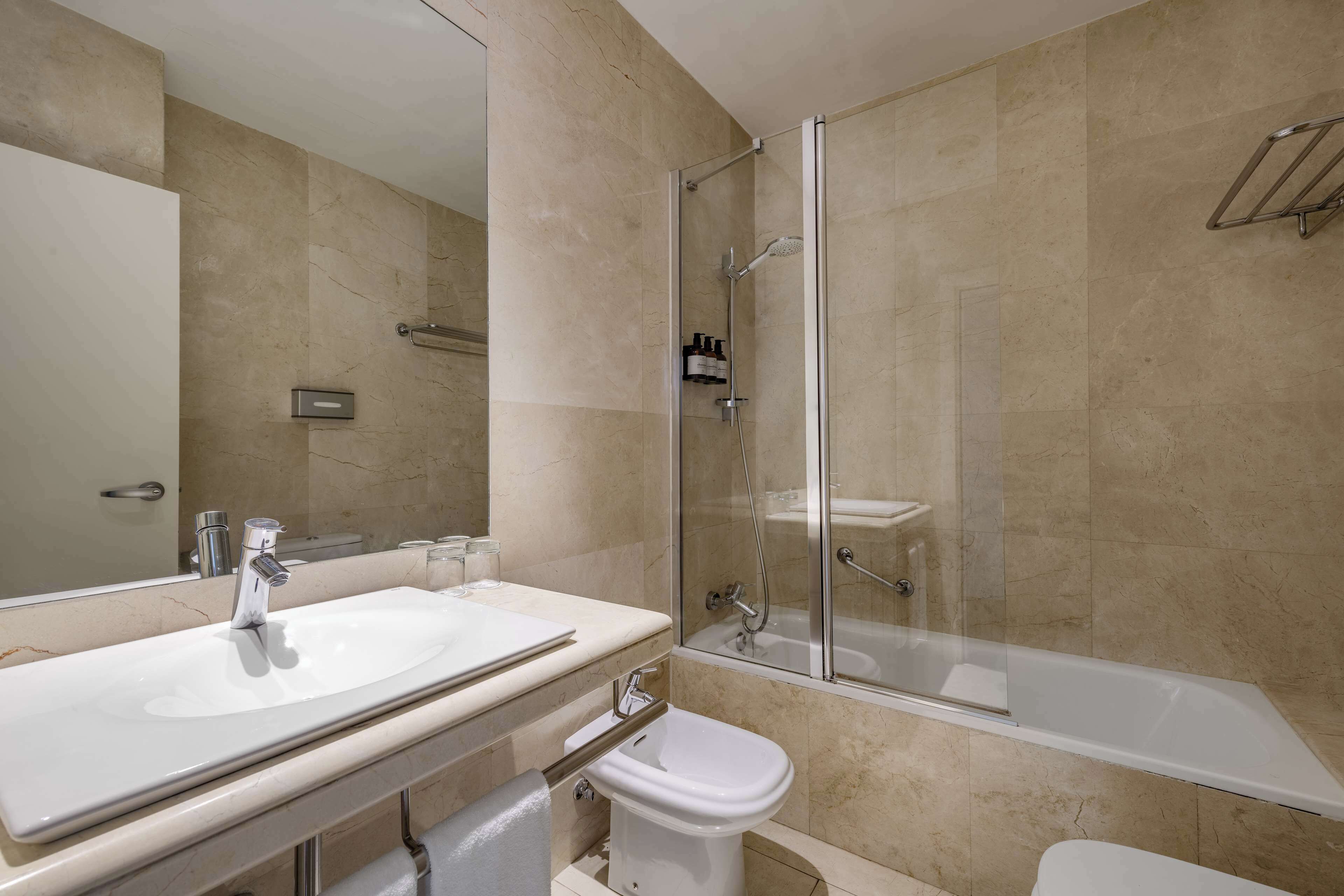 Een moderne badkamer met een groot wastafelmeubel, een douchecabine met glazen wanden en een apart toilet.
