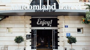 Entrada de un hotel con un letrero que dice 'Maland Bar Hotel and Bar' y '¡Disfruta!'. Hay dos macetas a cada lado de la entrada.