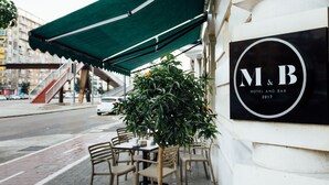 Un área de estar al aire libre con mesas y sillas, un toldo verde y un cartel que dice 'M&B Hotel and Bar 2017'.