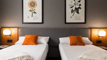 Une chambre d’hôtel avec deux lits, chacun doté de draps blancs et d’oreillers orange, ainsi que deux lampes fixées au mur.