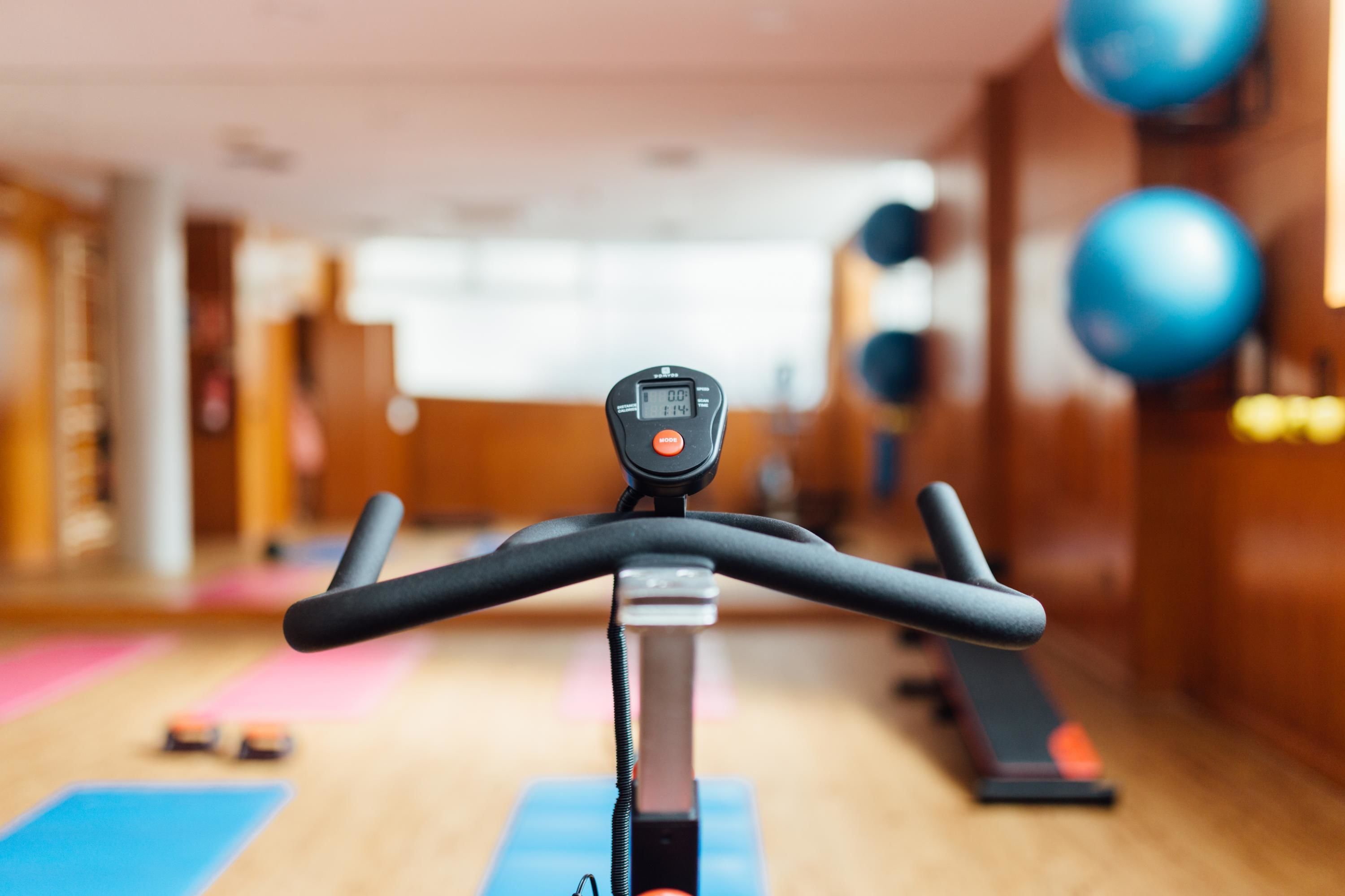 Una bicicleta estática en un gimnasio, con una pantalla digital, pelotas de ejercicios y colchonetas de yoga.