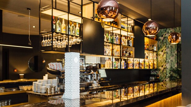 Zona de bar con estantes llenos de botellas, copas y una barra de mármol.
