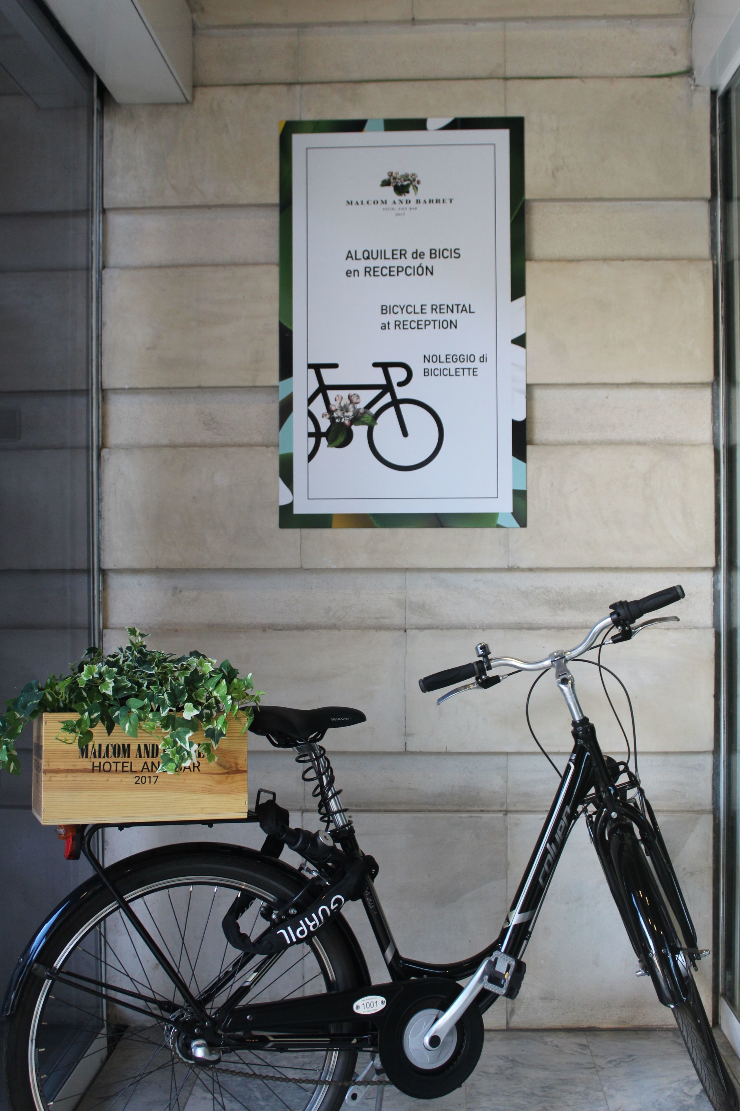 Un letrero de alquiler de bicicletas y una jardinera de madera con plantas verdes en una pared de edificio.