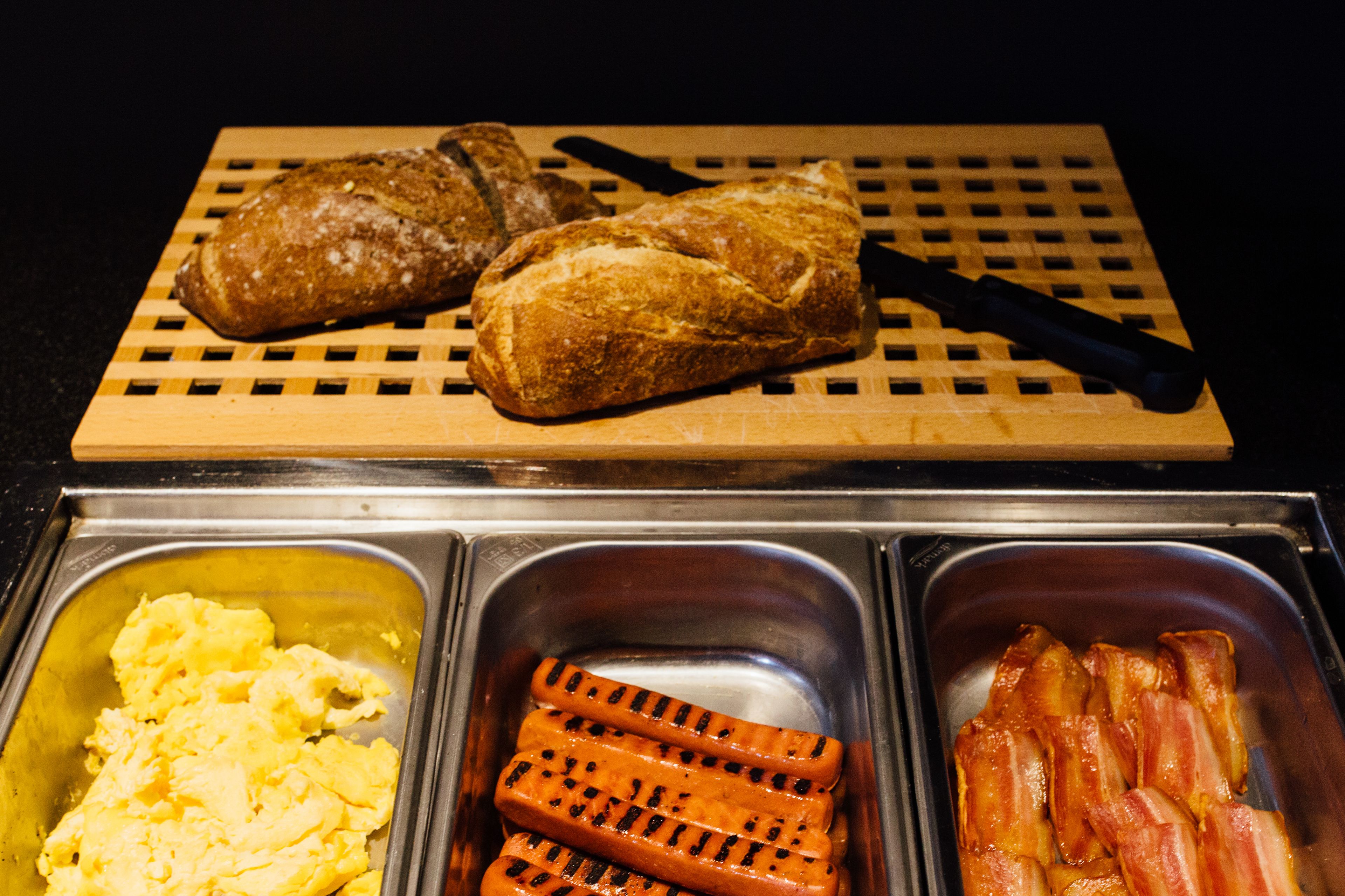 A breakfast buffet with scrambled eggs, grilled sausages, and bacon.
