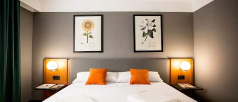 A hotel room with a large bed, two nightstands, two wall-mounted lamps, and two framed botanical prints.