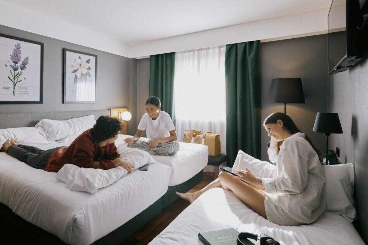 Habitación de hotel con dos camas, un escritorio, una lámpara e impresiones botánicas enmarcadas en la pared.
