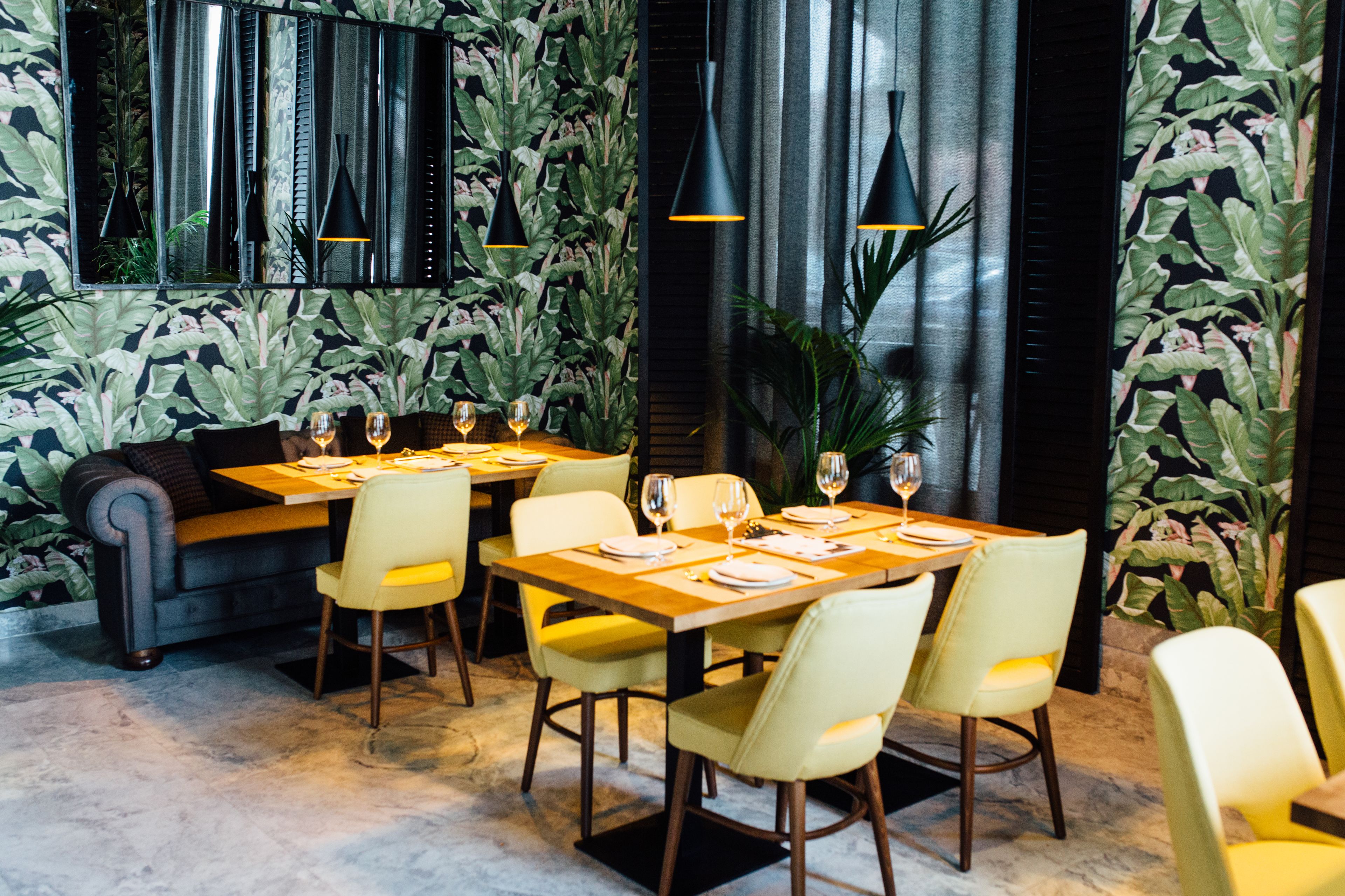 A restaurant with a modern interior, featuring a long table set for dining, yellow chairs, and black pendant lighting.