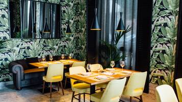 A restaurant with a modern interior, featuring a long table set for dining, yellow chairs, and black pendant lighting.