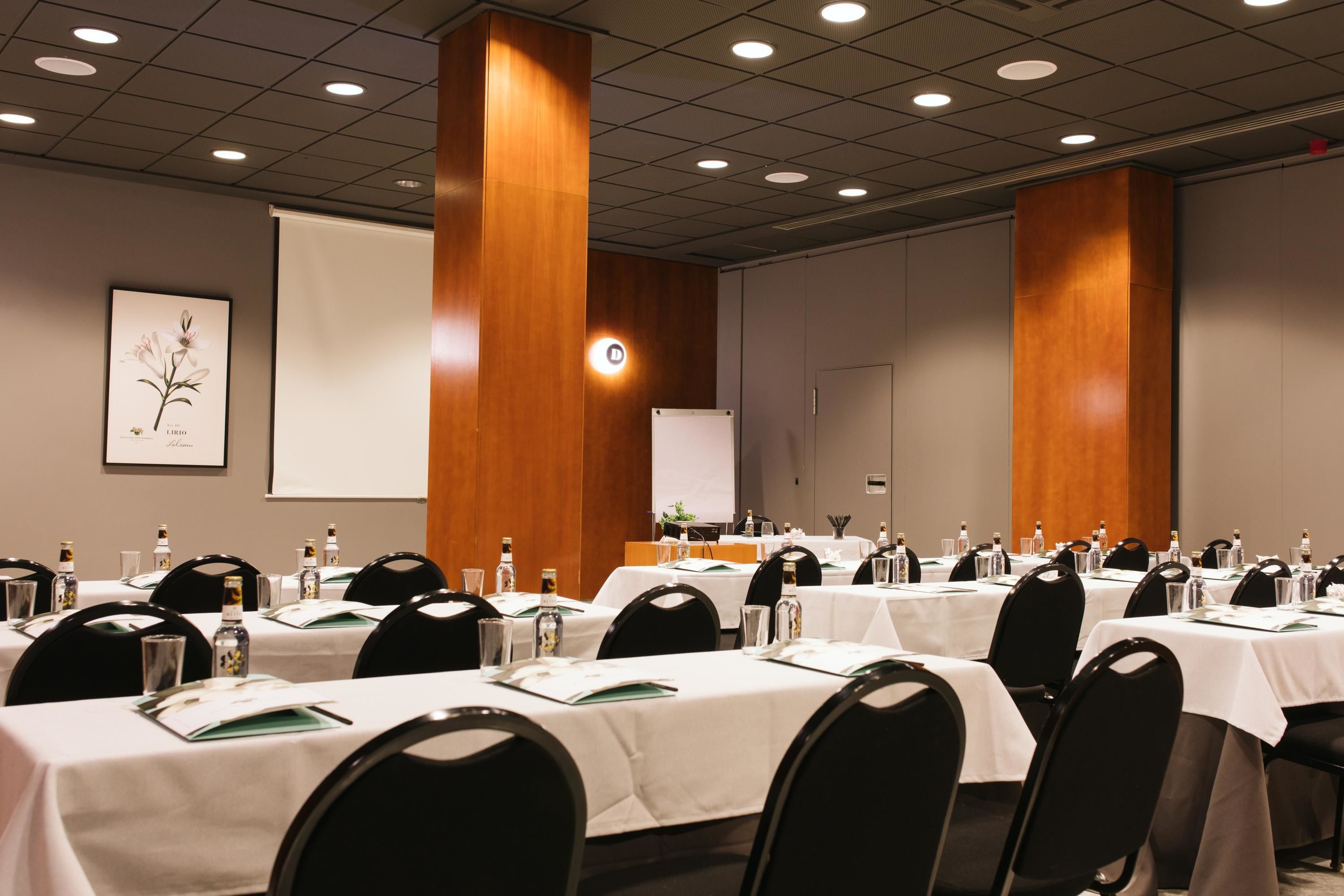 A conference room with multiple tables, chairs, and a projector screen.