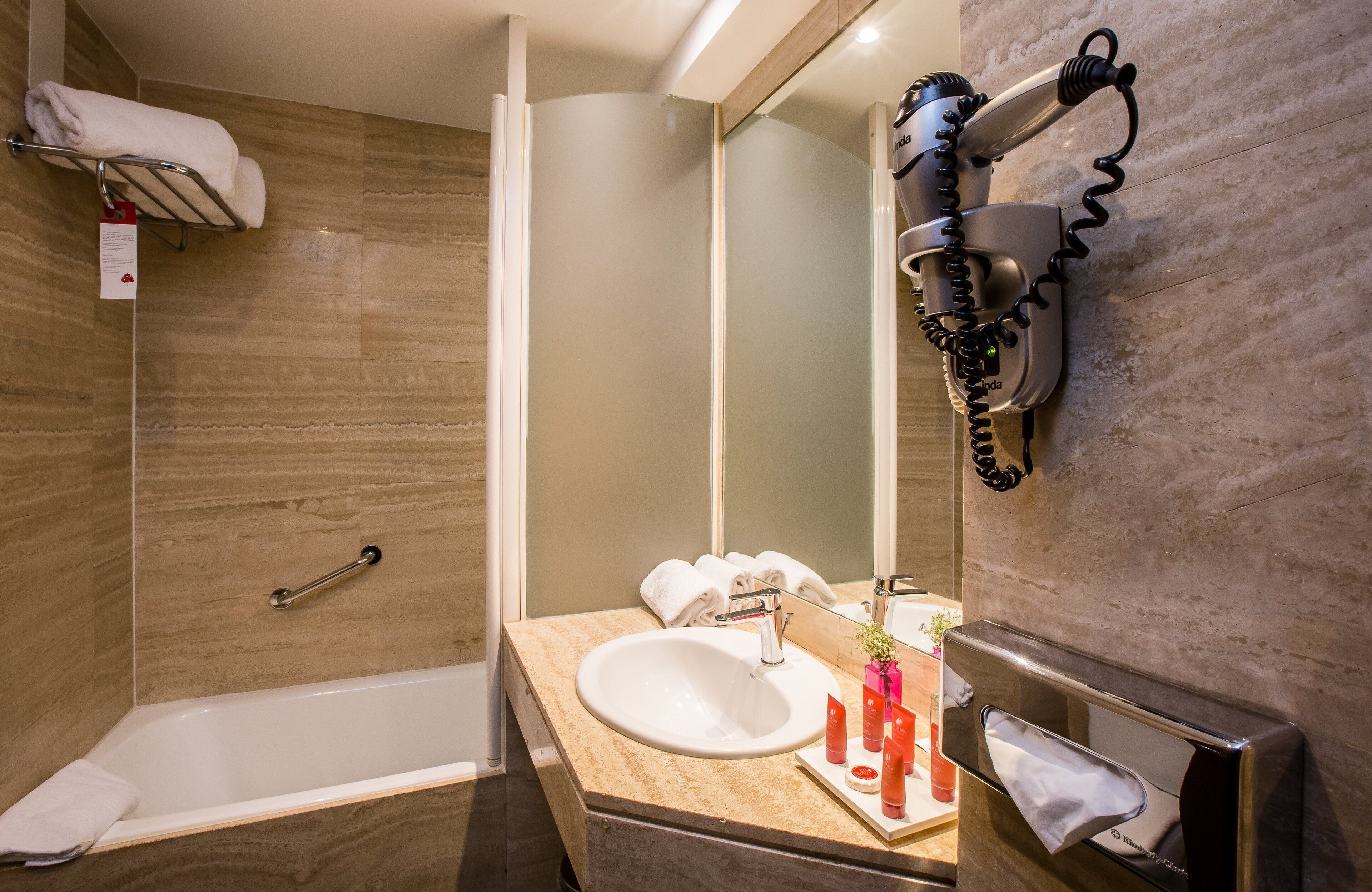 A modern bathroom with a bathtub, a sink, a towel rack, and a hairdryer mounted on the wall.