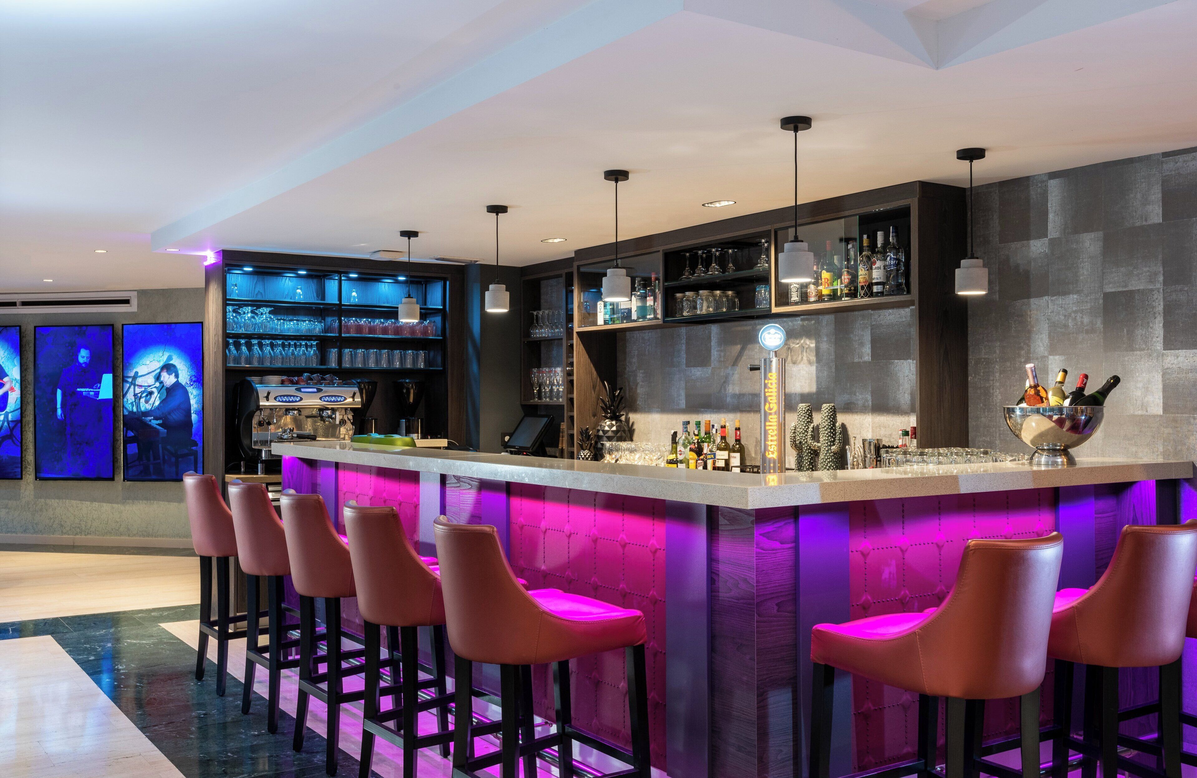 A modern bar area with a bar counter, multiple stools, and shelves stocked with bottles and glasses.