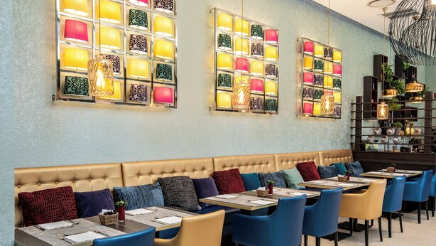 Ein Restaurantinneres mit einer langen Sitzbank, mehreren Tischen mit Stühlen und dekorativen Wandleuchten.