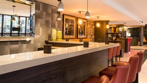 Een moderne bar met een lange toonbank, hangende verlichting en een zithoek met comfortabele stoelen.