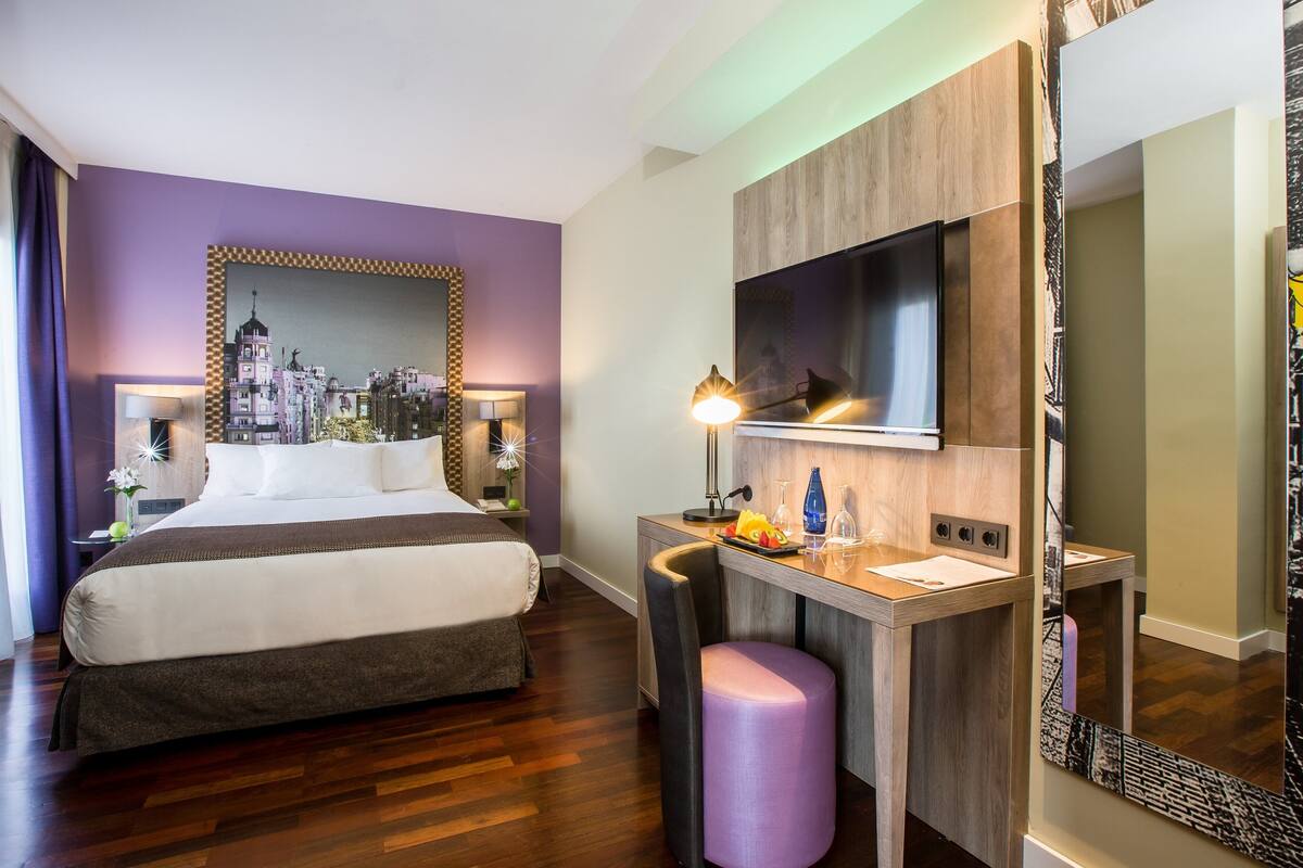 Une chambre d’hôtel équipée d’un lit, d’un bureau, d’une chaise, d’un miroir et d’une télévision.