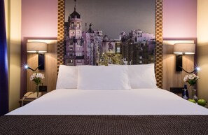 Une chambre d’hôtel avec un grand lit, deux lampes de chevet, un téléphone et une fresque murale représentant un paysage urbain.