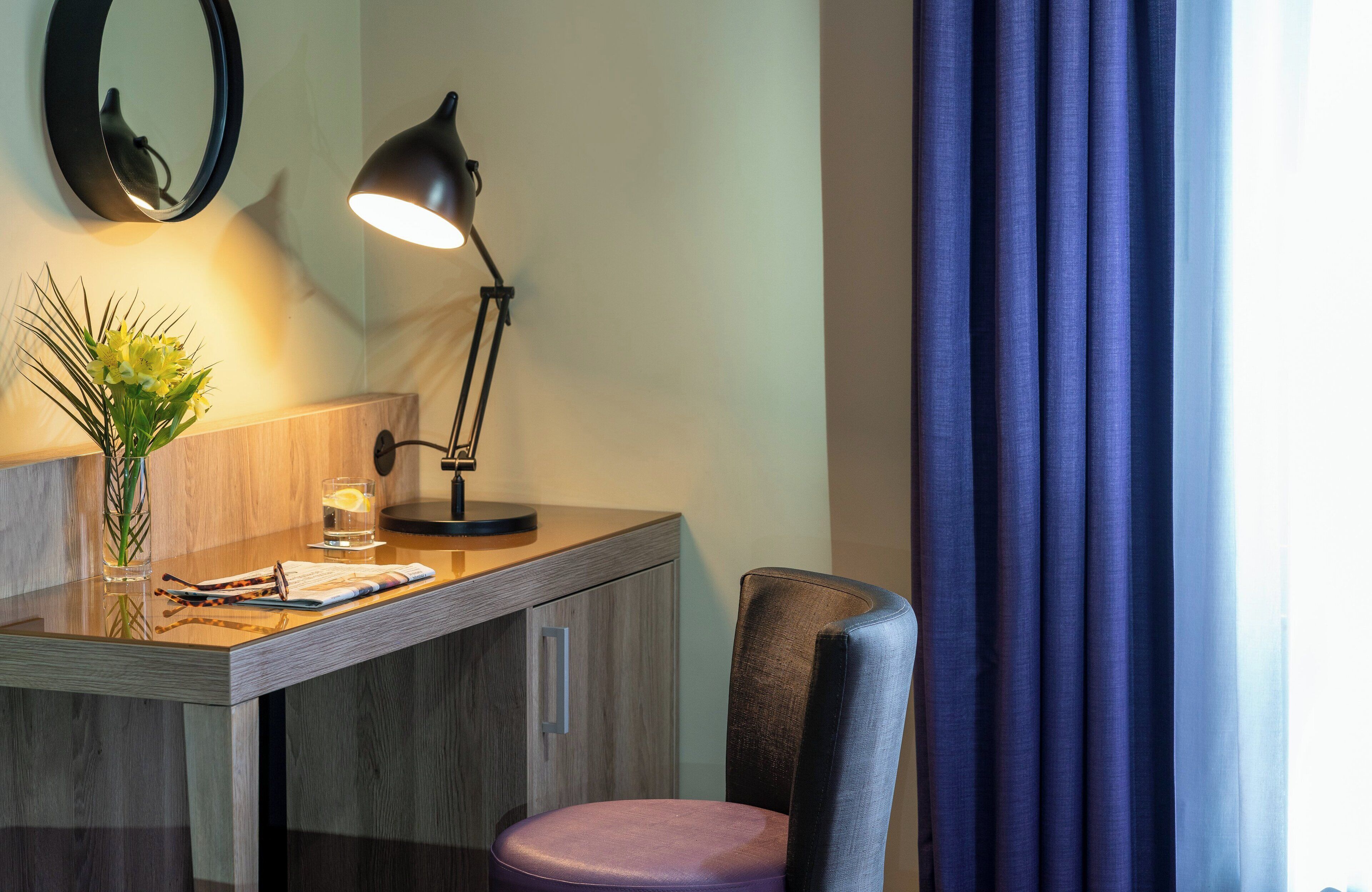 A desk with a lamp, a vase with flowers, and a glass of water.