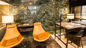 Een moderne hotelkamer met een marmeren wand, een houten bureau, twee leren fauteuils en een zwart marmeren salontafel.
