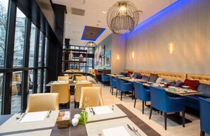 Un restaurant moderne avec des tables hautes, des chaises bleues et un coin salon confortable avec un canapé.