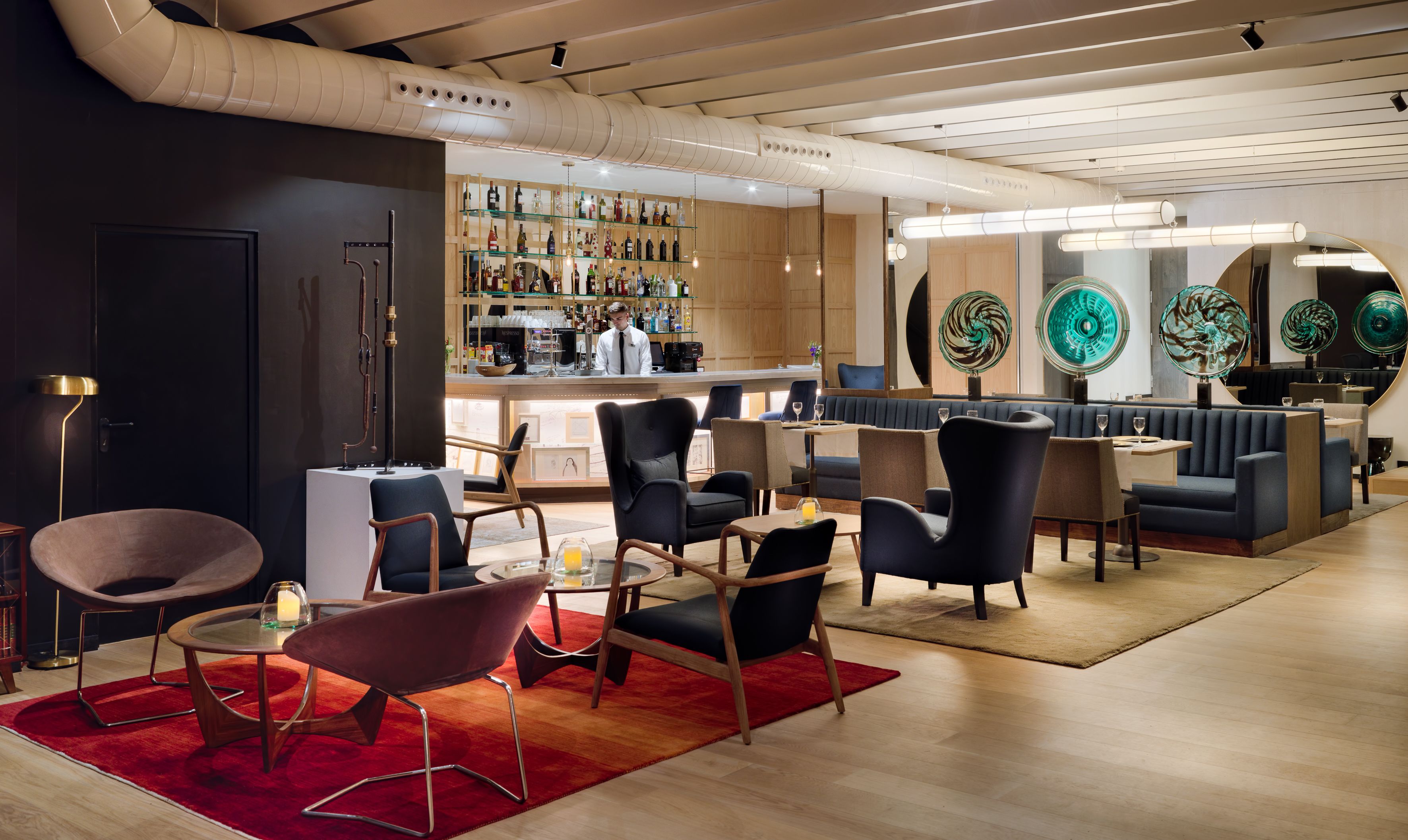 A modern bar area with a bartender, seating with round tables, and a wine display.