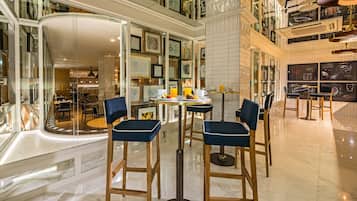 Un moderno vestíbulo de hotel con techo alto, paredes de vidrio y una mesa redonda central con sillas.