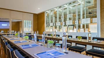 Un salón de conferencias con mesas largas, sillas y un muro de vidrio con cuadros enmarcados.