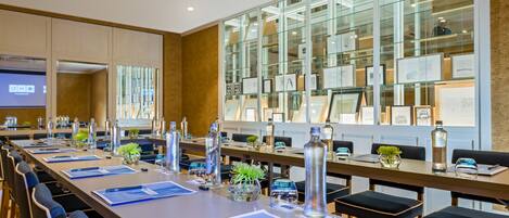 A conference room with long tables, chairs, and a glass display wall with framed pictures.