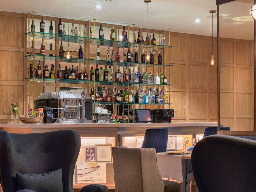Una zona de bar con varias estanterías llenas de botellas, una máquina de café y asientos con una mesa redonda.