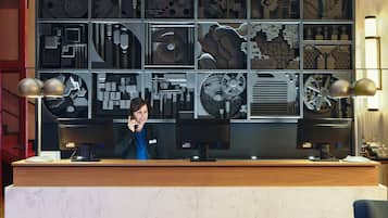 Mostrador de recepción con múltiples monitores, una barra de madera y una pared que exhibe diversos diseños arquitectónicos y mecánicos.