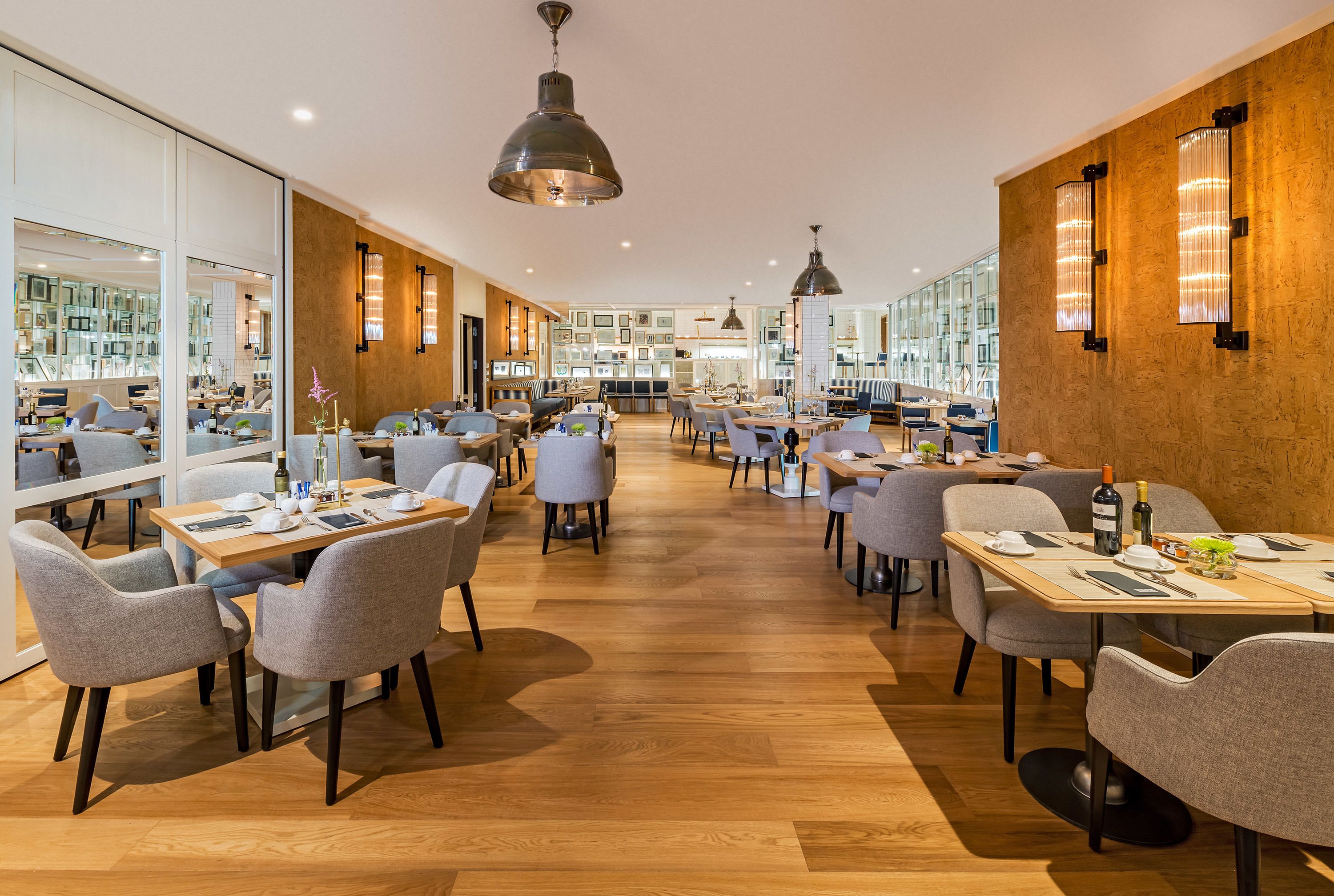 A modern restaurant with wooden floors, grey upholstered chairs, and tables set for dining.