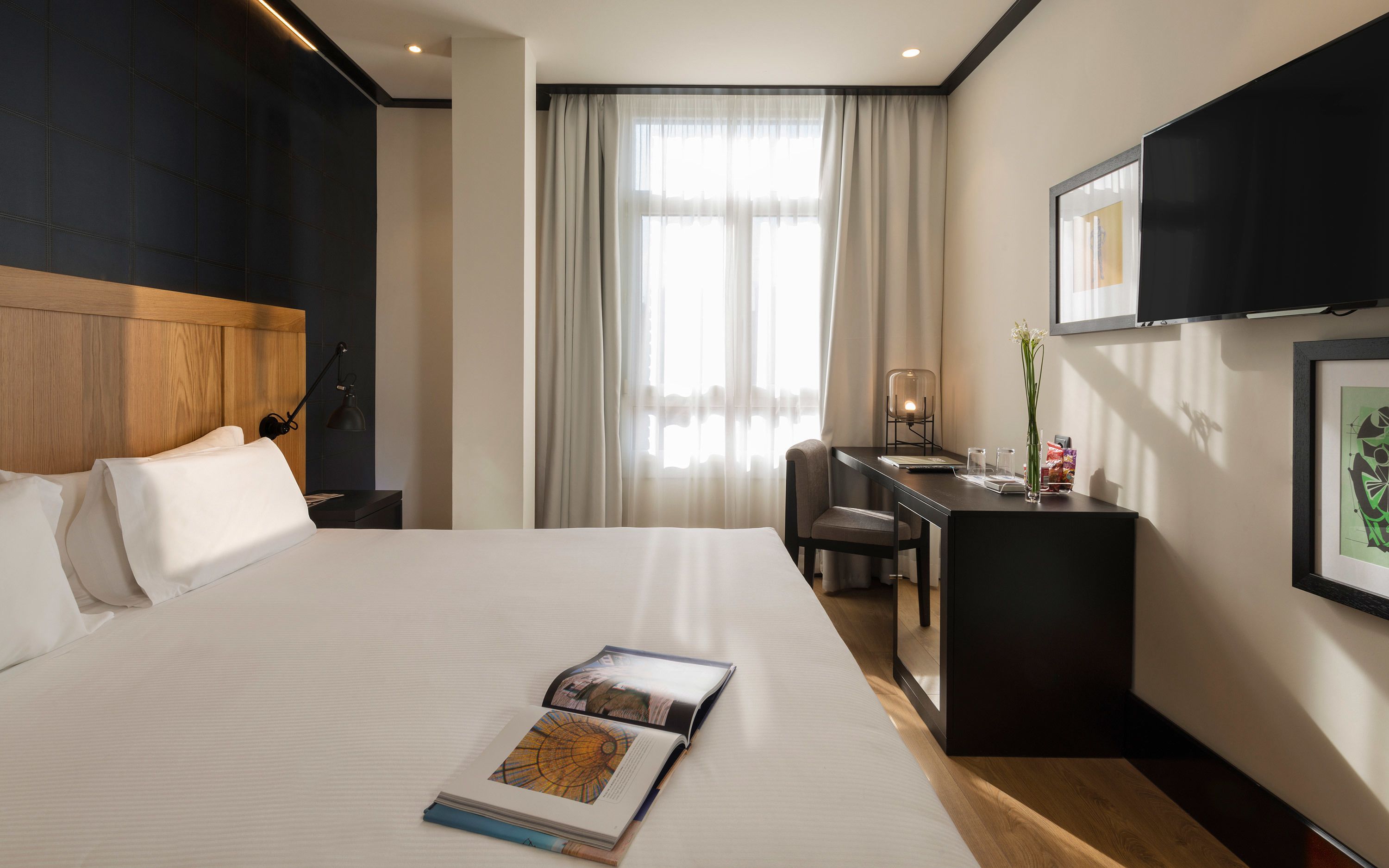 A hotel room with a large bed, a desk, a chair, a TV, and a window with curtains.