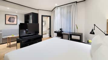 Una moderna camera d'albergo con un letto grande, una TV a schermo piatto, una scrivania con una lampada e un divano.