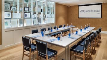 Konferenssihuone, jossa on pitkä pöytä, tuoleja ja projektorikangas, jolle heijastetaan tekstiä.