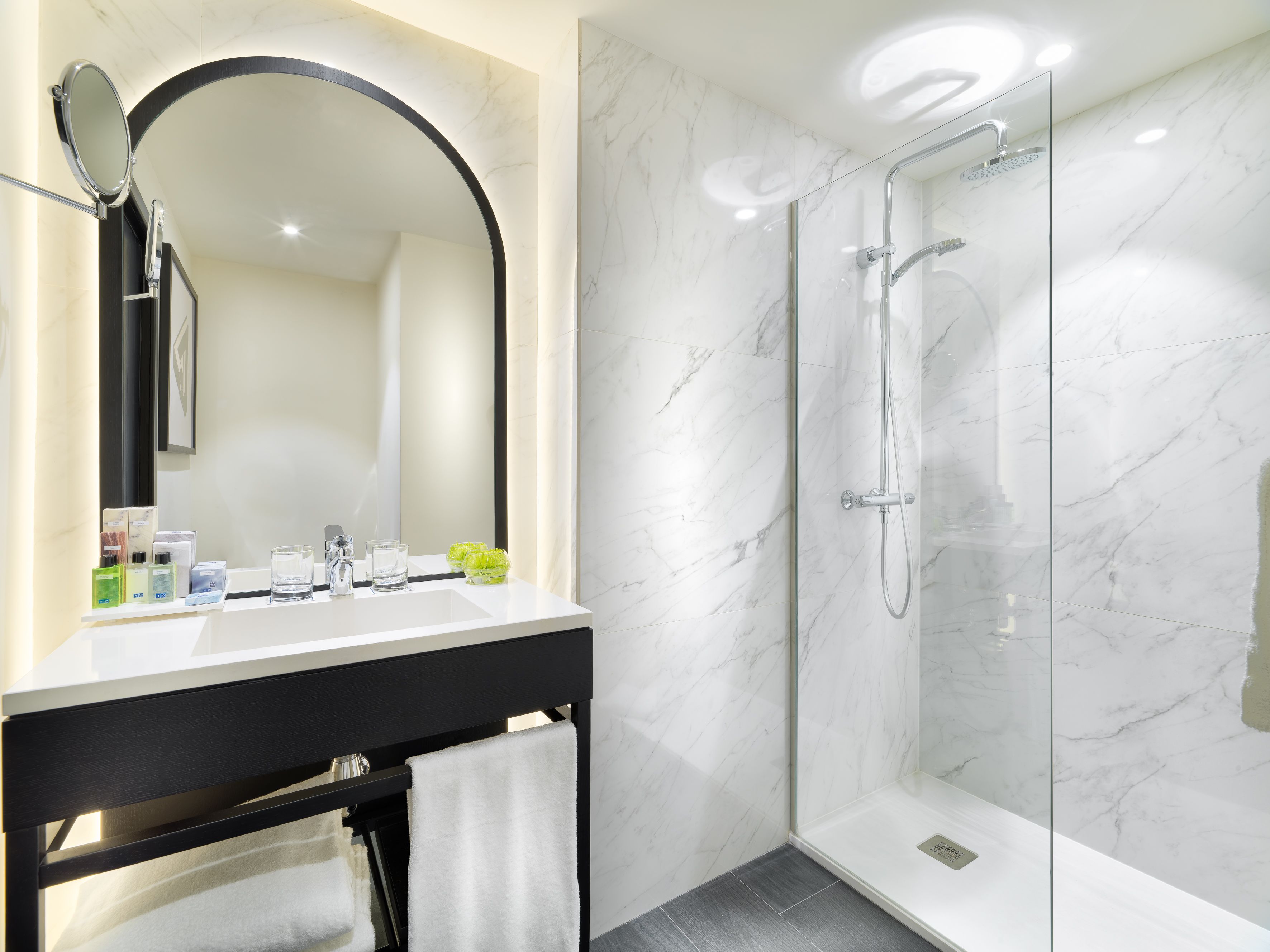 Une salle de bain moderne avec un meuble-lavabo en marbre, un grand miroir et une douche à parois de verre.