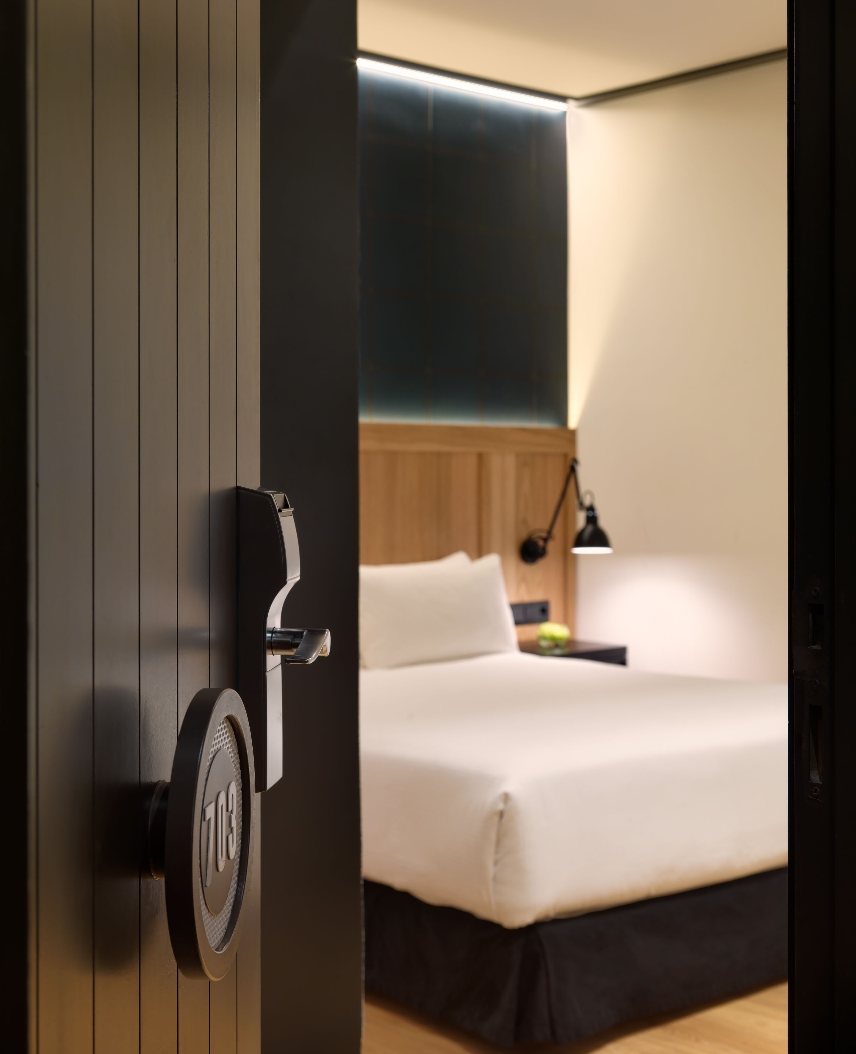 Quarto de hotel moderno com uma cama, uma escrivaninha e uma porta com fechadura.